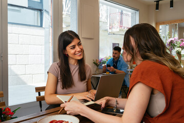 Two Women Reading and Working Together at a Café Table with Food

