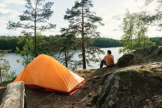 Camper Sitting by Lake with Orange Tent