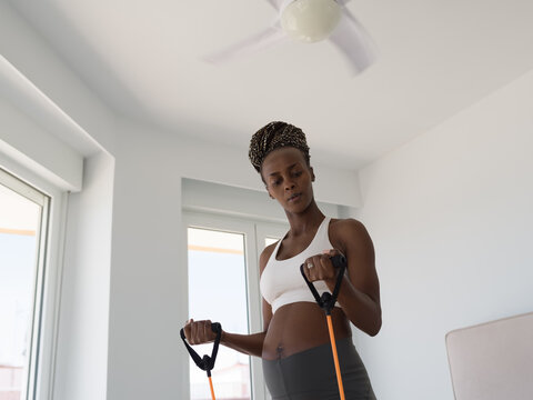 Focused pregnant woman exercising with expander at home