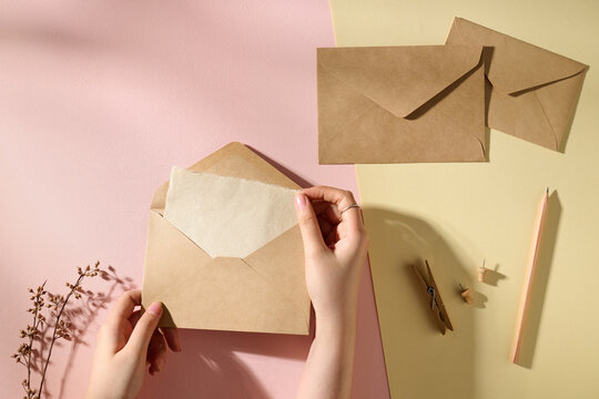 Hands Holding Brown Envelope with Handcrafted Paper on pink background