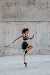 Fototapeta premium Young Hispanic woman jumping and exercising in sportswear outdoors in urban area in Latin America