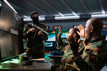 Masked terrorist holding assault rifle invading enemy base of operations, threatening soldiers with...