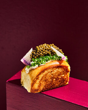 Caviar Brioche Bread Bite Perched on Red Plank with Burgundy Backdrop
