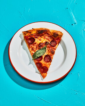 Overhead of One Slice of Pepperoni Pizza on Blue backdrop