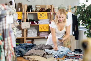 Young woman scans QR code and label of trousers or shorts using mobile phone camera. Customer client is interested in country of origin of product, checks certificate on consumer protection website..