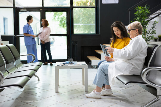 Doctor and asian woman in a discussion over radiography test results in a hospital lobby area. Medical specialist offering professional guidance in order to create a treatment plan.