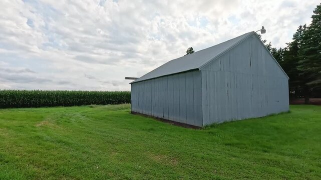 Gray Pole Barn Shed with Evergreen Trees and Cornfield, Handheld Pan Including Auger and Edge of Grain Bin