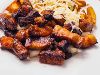 A plate of food with mini pork belly slices and potatoes and cheese and a fork and knife on a table. Scene is casual and inviting. Tasty simple food.