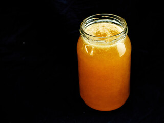 Glass jar of golden bee honey is on a dark background. Fine organic product concept. Agriculture and food industry.