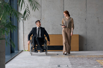Director in a Wheelchair Engaging in a Business Discussion with a Colleague While Navigating a Modern Office