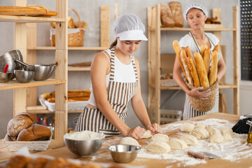 Skilled successful bakers in uniform working in light bakery. Young girl working with pieces of...