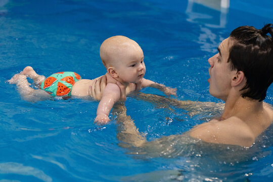 Newborn swimming with a swim coach in the swimming pool. Swimming lessons. - Powered by Adobe