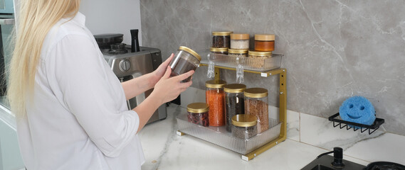 A woman in a white shirt organizes her kitchen counter, placing a spice jar onto a stylish...