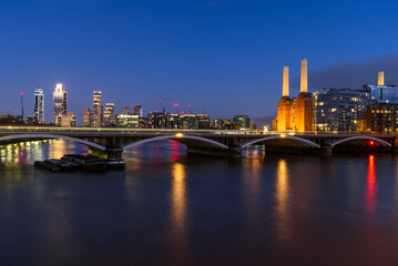 View of Battersea power station and  Vauxhall skyline in London at twilight in winter. Light trails left by a train passing over a bridge are visible in foregound.