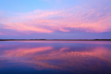 Obraz premium Serene lake reflecting a vibrant pink and purple sunset sky with a distant shoreline view ahead