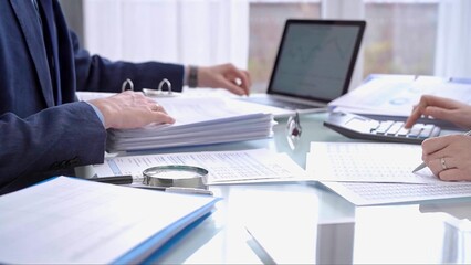 Business colleagues accountants or auditors reviewing financial data in office. Two professionals analyzing paper reports and using calculators. Audit and taxes