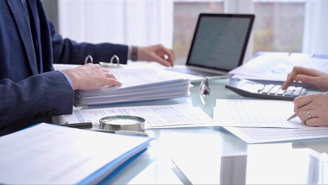 Business colleagues accountants or auditors reviewing financial data in office. Two professionals analyzing paper reports and using calculators. Audit and taxes