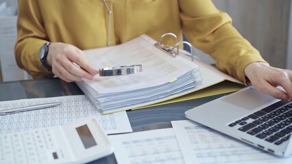Female auditor in business attire inspecting financial reports with magnifying glass, surrounded by documents and a laptop and calculator. Business audit and taxes concept