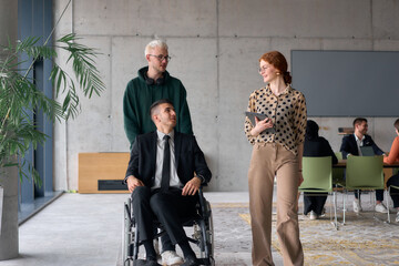 A diverse team of business colleagues, including a director in a wheelchair, engages in a collaborative discussion as they move together through a modern office space
