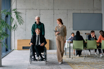 A diverse team of business colleagues, including a director in a wheelchair, engages in a collaborative discussion as they move together through a modern office space