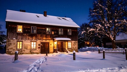 Fototapeta premium A cozy, snow-covered wooden house at night with illuminated windows, surrounded by snowy grounds