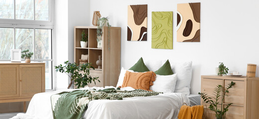 Interior of stylish bedroom with cozy bed, houseplants and beautiful paintings