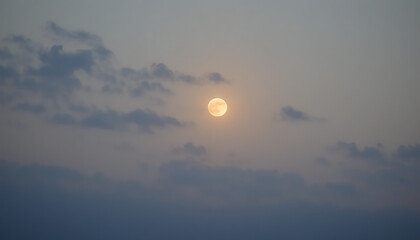 Full moon peeking through hazy, light gray clouds.