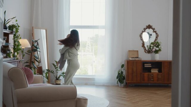 Wide shot shows mother with open arms embracing her two year old son in a bright living room. A tender lifestyle scene highlighting love, family joy, and everyday happiness at home. High quality 4k