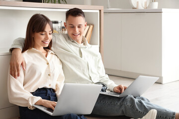 Young couple using laptops on floor in kitchen