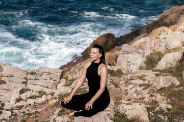 Woman practicing meditation on rocky coastline, surrounded by ocean waves, embodying tranquility and mindfulness in a serene natural environment with copy space