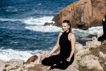 Woman practicing meditation in a serene coastal environment, surrounded by rocks and ocean waves, embodying tranquility and mindfulness with copy space