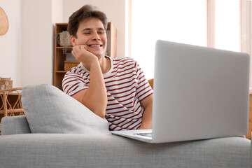 Fototapeta premium Young man video chatting with laptop on sofa at home