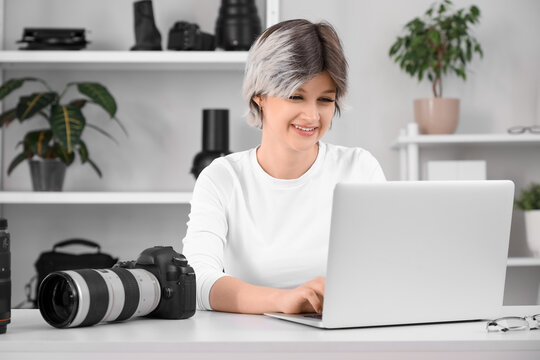 Beautiful young happy female photographer with professional camera and laptop working at table in studio