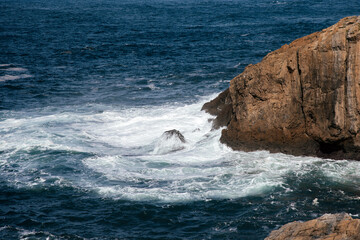 Ocean waves crashing against rocky cliffs, creating a dynamic seascape with foamy surf and deep blue water, embodying the power of nature and tranquility