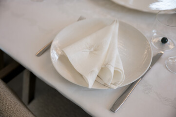 Elegant table setting with white plate, folded napkin, cutlery, and glass, creating a refined and minimalist dining atmosphere for celebrations or fine dining.