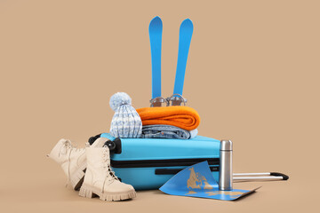 Suitcase with winter accessories, skis and map on beige background