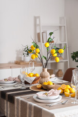 Stylish table setting decorated with many fresh citruses and beautiful lemon tree branches in dining room