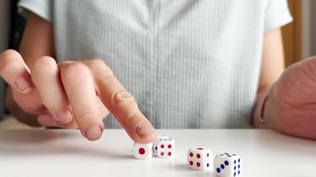 Close up video of a woman playing a dice game on a white table. Rolling cubes with numbers, chance, gambling, board game elements, luck and entertainment concept