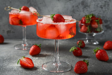 Glasses of drink with ice cubes and strawberries on grey grunge background