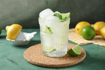 Glass of drink with lime slices, ice cubes and mint leaves on green grunge background