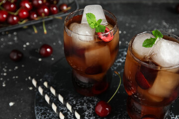 Glasses of drink with cherry, ice cubes and mint leaves on black grunge background