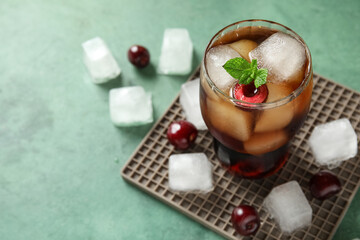 Glass of drink with cherry, ice cubes and mint leaves on green grunge background