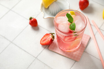 Glass of drink with ice cubes, mint leaves, strawberry and lemon slices on white tile background