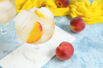 Glass of drink with ice cubes and peach slices on blue grunge background