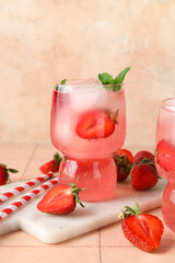 Glass of tasty cold cocktail with strawberry on pink tile table near wall, closeup
