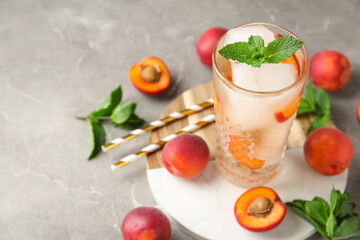 Glass of tasty cold cocktail and apricots on grey grunge background, closeup