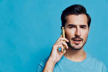 Young smiling man speaking on a mobile phone, wearing a light blue t-shirt, standing against a vibrant blue background, showcasing a casual lifestyle concept.