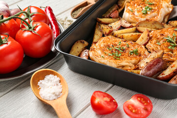 Baking dish with tasty baked cabbage steaks, potatoes, fresh tomatoes and spices on white wooden background