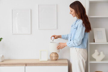 Beautiful young happy woman changing light bulb in stylish lamp on commode at home