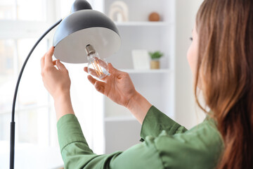 Beautiful young woman changing light bulb in floor lamp at home, closeup